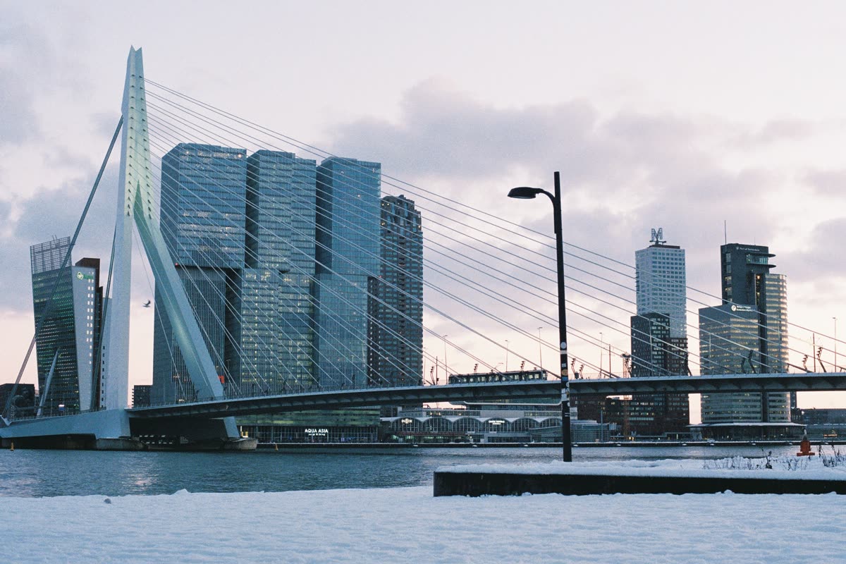 The Erasmus Bridge and the towers of Kop van Zuid seen across the Maas, with snow on the quay